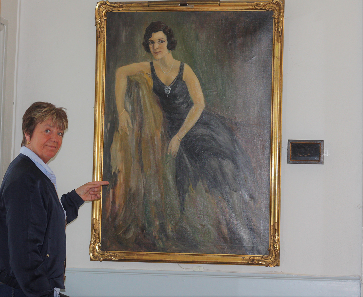 Birgitta står framför en porträttmålning av slottsfrun Marja Hedberg Braathen.